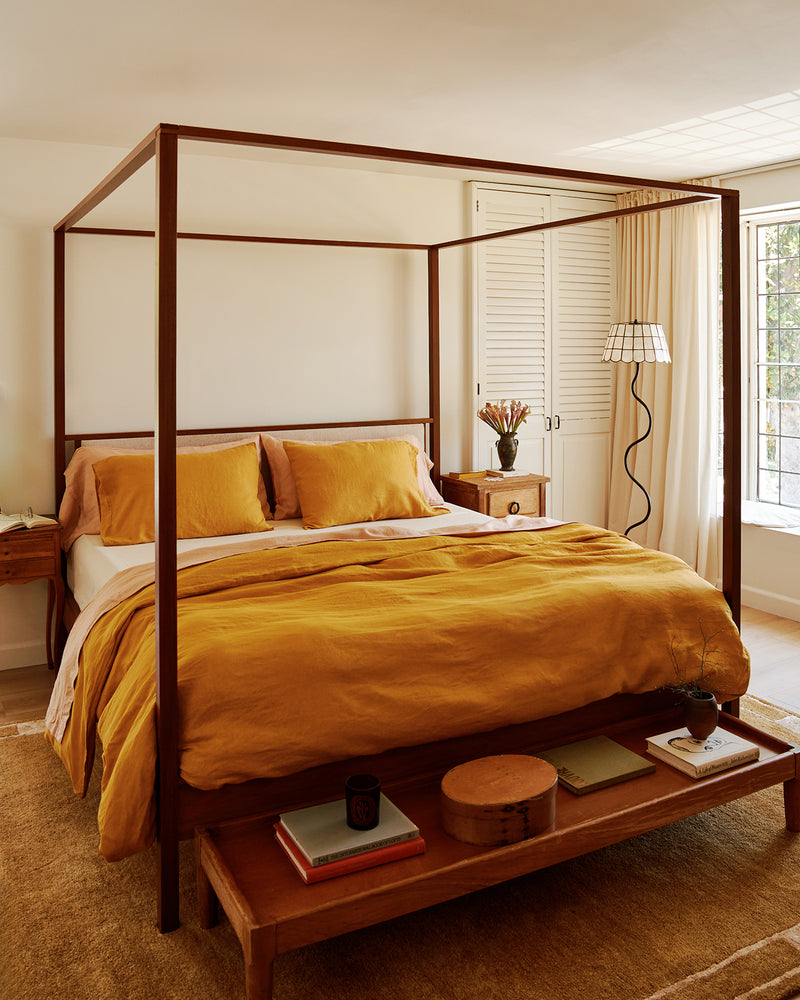 Bedroom with a wooden canopy bed and 100% french flax linen bedding in turmeric, terracotta and creme.