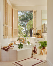 Bathroom with a large window, bathtub, and plants with the two-toned bath towels in cacao and creme resting on bath tub. - view