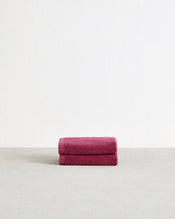 The Berry 100% Cotton Terry Face Washers (Set of Two) by Bed Threads feature soft, absorbent magenta towels with stitched edges and white tags, stacked on a light textured surface—ideal for durable daily face cleansing. - view