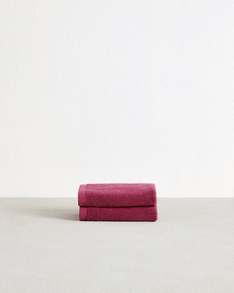 The Berry 100% Cotton Terry Face Washers (Set of Two) by Bed Threads feature soft, absorbent magenta towels with stitched edges and white tags, stacked on a light textured surface—ideal for durable daily face cleansing.