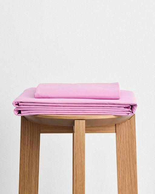 The Bubblegum Organic Cotton Sheet Set by Bed Threads is neatly folded and placed on a wooden stool against a plain white background.