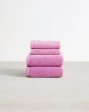 Set of two bubblegum pink face washers and two hand towels in 100% cotton terry stacked on a light grey surface with a white background.  - view