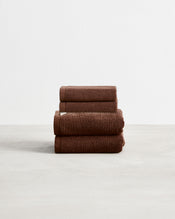 A stack of two, organic cotton terry hand towels and two face washers in an espresso brown shade. - view