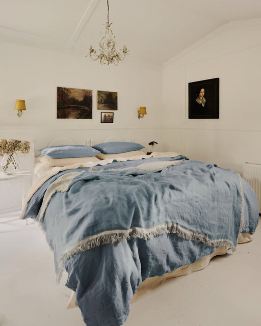 Bedroom with blue bedding, moody artworks on the walls and a chandelier