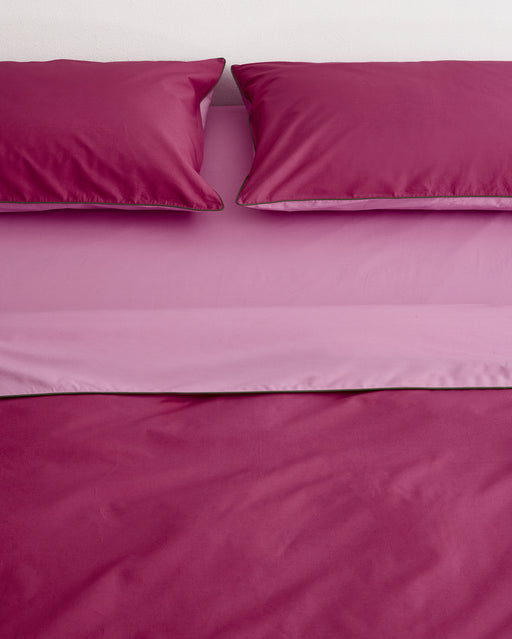 A neatly made bed features two dark pink pillows and the Bed Threads Berry, Bubblegum & Moss Piped 100% Organic Cotton Duvet Cover, paired with lighter pink fitted and flat sheets beneath the pillows.