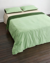 A neatly made bed with light green sheets, matching pillowcases, and a dark green accent strip across the top, set on dark wooden flooring against a white wall. - view