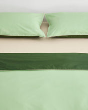 A neatly made bed with light green pillows and bedding, a beige sheet, and a dark green decorative band across the bed. The scene is minimal and the colors are soft and calming. - view