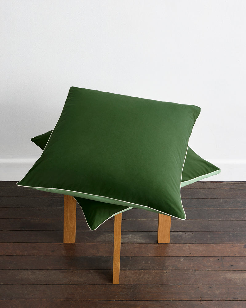 A neatly made bed features Bed Threads' Moss, Apple & Vanilla Piped 100% Organic Cotton European Pillowcases (Set of Two) in light green, paired with dark green shams and a runner, all set against a wooden headboard.