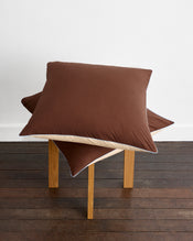 A neatly made bed features Bed Threads’ Espresso, Vanilla & Sky Piped 100% Organic Cotton European Pillowcases alongside matching sheets and duvet, all GOTS-certified for comfort, set against a wooden headboard. - view
