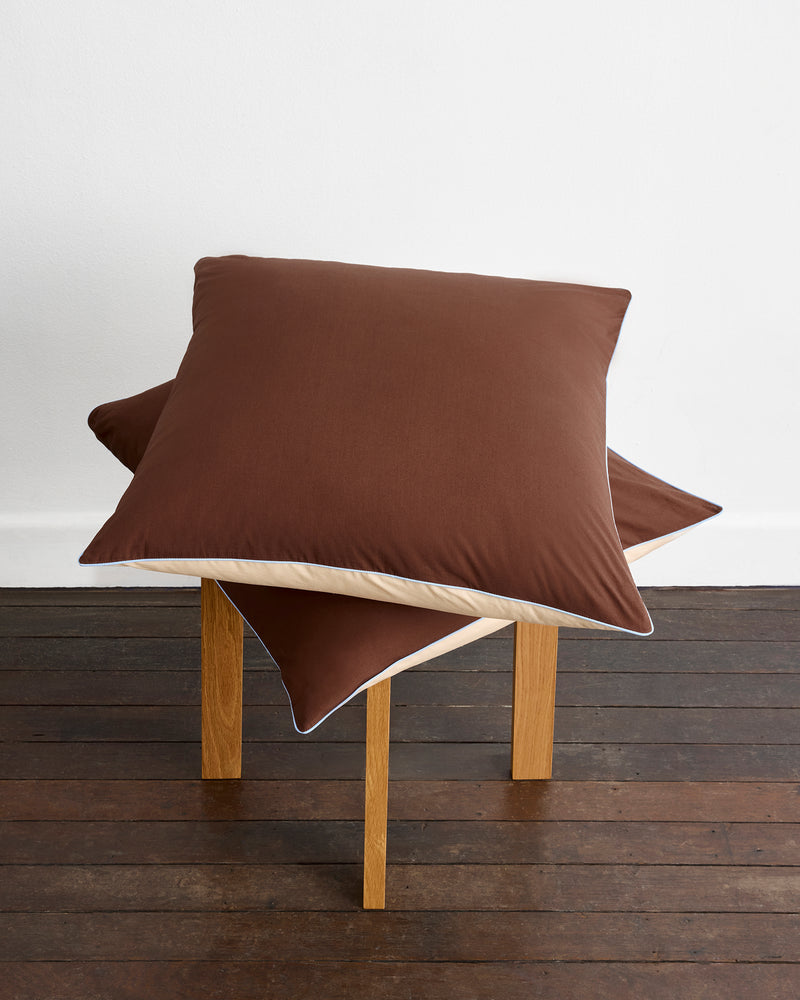 A neatly made bed features Bed Threads’ Espresso, Vanilla & Sky Piped 100% Organic Cotton European Pillowcases alongside matching sheets and duvet, all GOTS-certified for comfort, set against a wooden headboard.