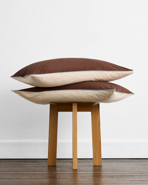 A neatly made bed features Bed Threads’ Espresso, Vanilla & Sky Piped 100% Organic Cotton European Pillowcases alongside matching sheets and duvet, all GOTS-certified for comfort, set against a wooden headboard.
