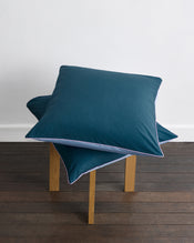 A bed with matching bedding features two Aegean and two Sky & Bubblegum Piped 100% Organic Cotton European Pillowcases by Bed Threads, all with contrasting trim, arranged neatly against a wooden headboard. - view