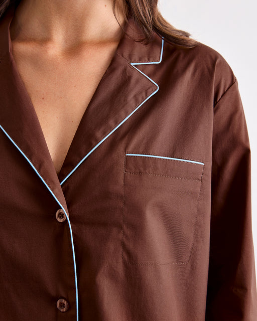A close-up of a person wearing the Bed Threads Espresso & Sky Piped Long Sleeve Shirt, featuring white contrast piping along the collar, pocket, and edges. This cotton shirt has a smooth finish and includes a chest pocket.