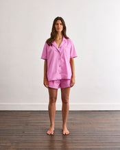 A person wearing the Bubblegum & Berry Piped Short Sleep Set by Bed Threads stands indoors; only their lower torso and upper legs in the elastic-waist shorts are visible. - view