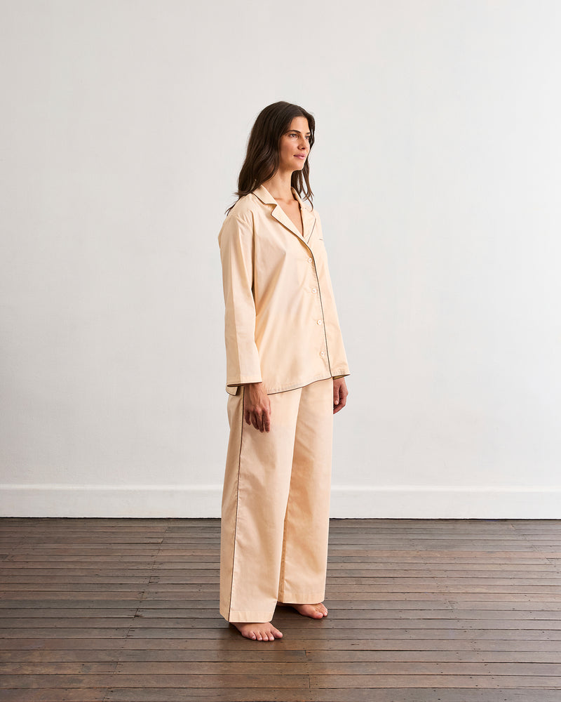 A woman stands barefoot on a wooden floor, wearing Bed Threads’ Vanilla & Espresso Piped Pants, crafted from breathable cotton with a relaxed fit and elasticated waist, set against a plain white wall.