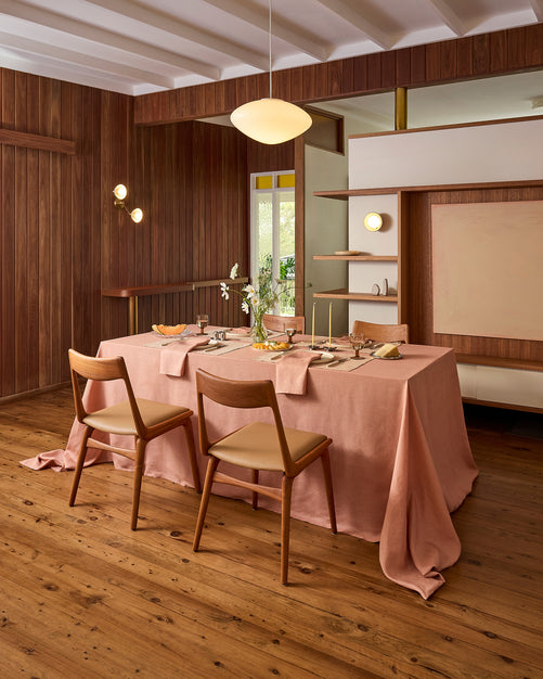 A white plate with crossed fork and knife rests on a Bed Threads Terracotta 100% French Flax Linen Placemat atop a rustic wooden table, with a spoon to the right and a clear glass above for stylish table protection.