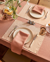 A table set for two with the Hazelnut & Terracotta 100% French Flax Linen Table Bundle by Bed Threads, white plates, pink napkins, silver cutlery, amber glassware, flowers, lemons, and salt and pepper shakers creates a cozy dining scene. - view