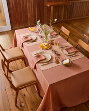 A white plate with crossed fork and knife rests on a Bed Threads Terracotta 100% French Flax Linen Placemat atop a rustic wooden table, with a spoon to the right and a clear glass above for stylish table protection. - view