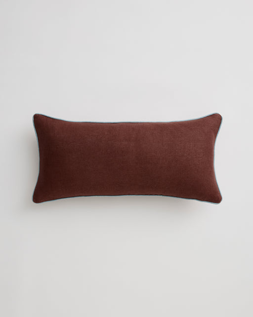 Close-up of the Bed Threads Cacao & Lagoon 100% French Flax Linen Lumbar Cushion Cover, featuring brown fabric with light blue contrast piping, resting on a white surface.