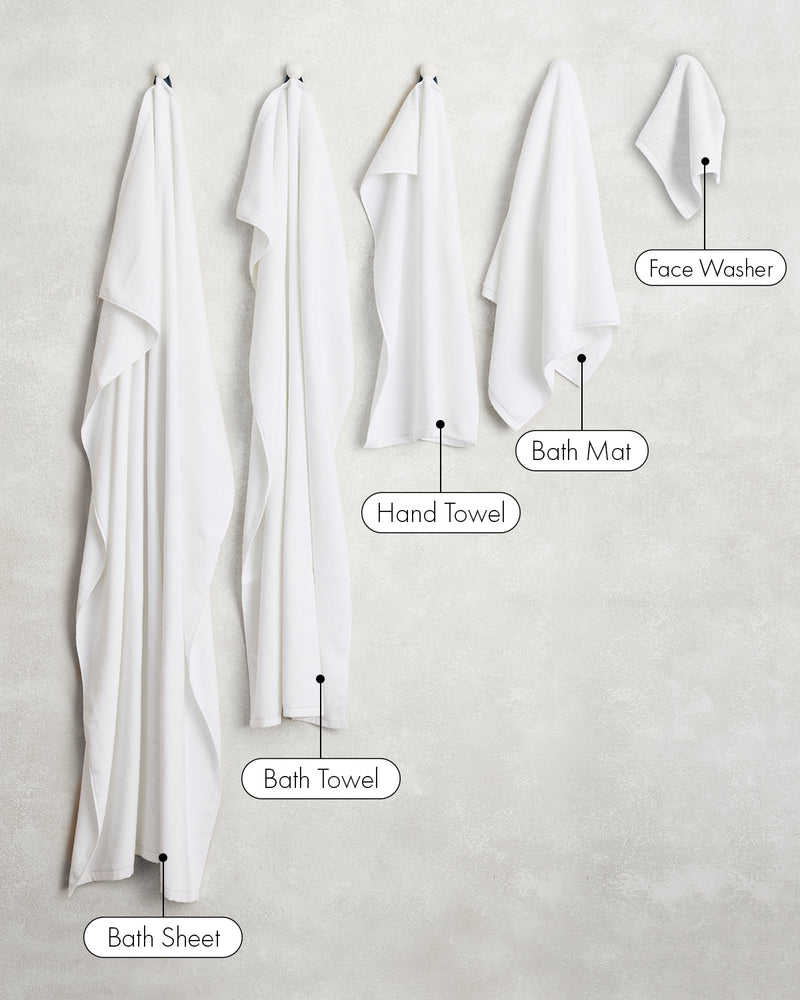 Two crisp white 100% cotton terry bath towels by Bed Threads hang on the wall, showcasing plush texture and absorbency—the perfect addition to your bathroom essentials.