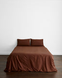 A close-up of the Bed Threads Espresso Organic Cotton shows smooth brown fabric with gentle folds and soft shadows, highlighting its subtle textured look.