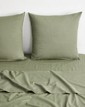 Olive green bedding set featuring a flat sheet and two matching pillowcases on a bed against a plain white wall. - view