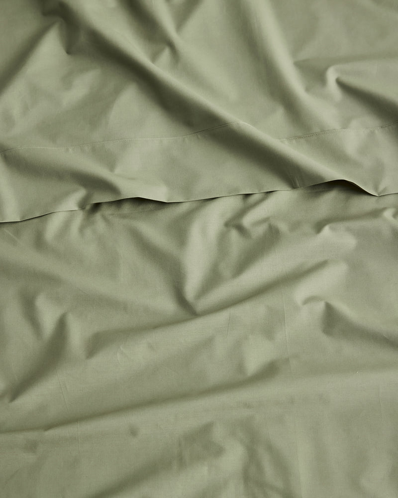 A close-up of organic cotton olive green sheets with soft folds and a horizontal seam, filling the entire frame.