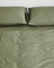 Organic cotton olive green duvet cover with two matching pillowcases on a bed against a plain white wall. - view
