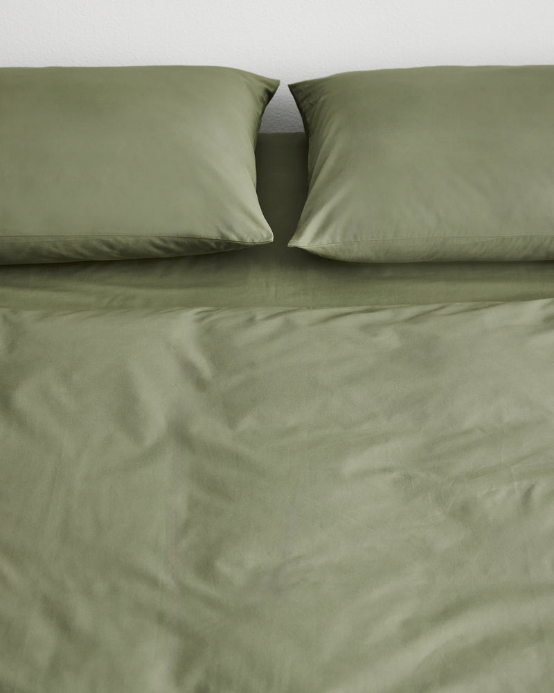 Organic cotton olive green duvet cover with two matching pillowcases on a bed against a plain white wall.