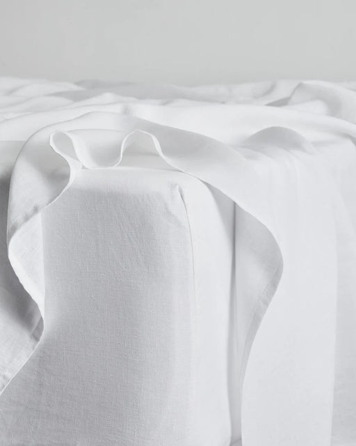 A close-up of a white bed with crisp, white sheets and a flat sheet draped loosely over the edge, creating a soft, minimal, and serene atmosphere.