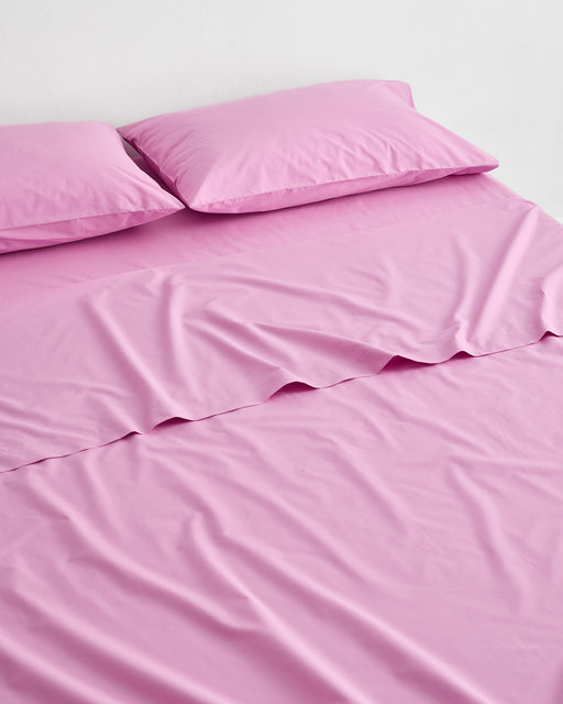A neatly made bed with two pillows, all dressed in matching bright pink Bubblegum Organic Cotton Fitted Sheet from Bed Threads, GOTS certified percale bedding, set against a plain white background.