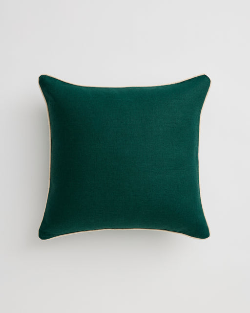A close-up of the Bed Threads Forest & Crème 100% French Flax Linen Piped Cushion Cover, in green with white piping, sits on a light grey surface.
