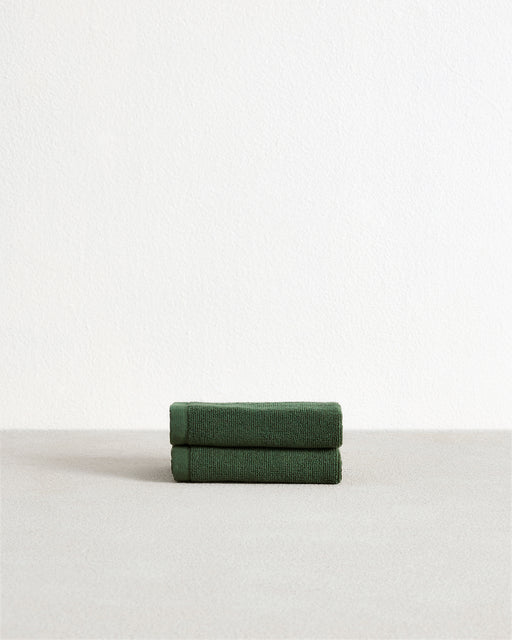 Set of two Moss 100% Cotton Terry Face Washers by Bed Threads, dark green with stitched edges and small corner labels, displayed on a light textured surface. Soft, absorbent, and ideal for daily facial care.