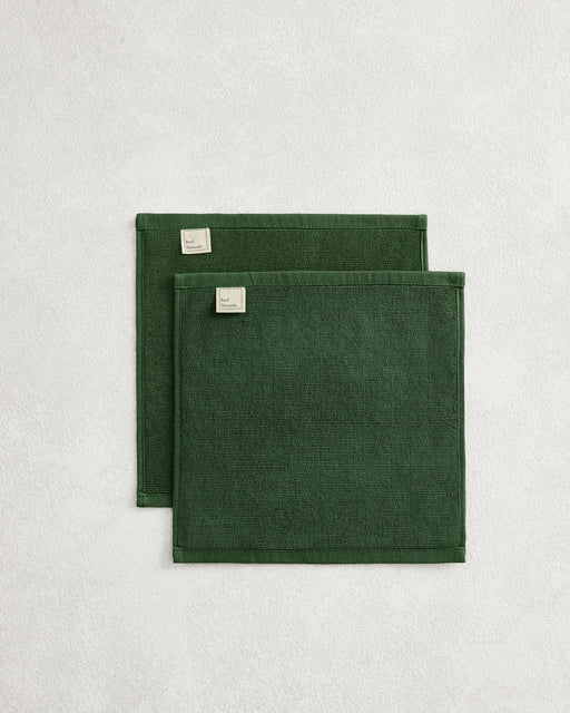 Set of two Moss 100% Cotton Terry Face Washers by Bed Threads, dark green with stitched edges and small corner labels, displayed on a light textured surface. Soft, absorbent, and ideal for daily facial care.