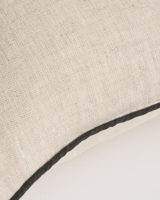 Close-up of the Bed Threads Oatmeal & Charcoal 100% French Flax Linen Piped Cushion Cover, showcasing beige linen with visible charcoal piping along the curved edge against a plain white background.