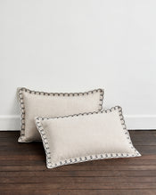 A pair of Bed Threads Oatmeal & Charcoal 100% French Flax Linen Swirl Pillowcases rests on a dark wooden floor against a plain white wall. - view