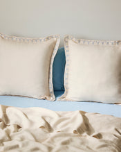 Two Crème & Coast 100% French Flax Linen Swirl European Pillowcases by Bed Threads rest against a light blue headboard, paired with a light beige sheet and soft natural lighting for an inviting look. - view