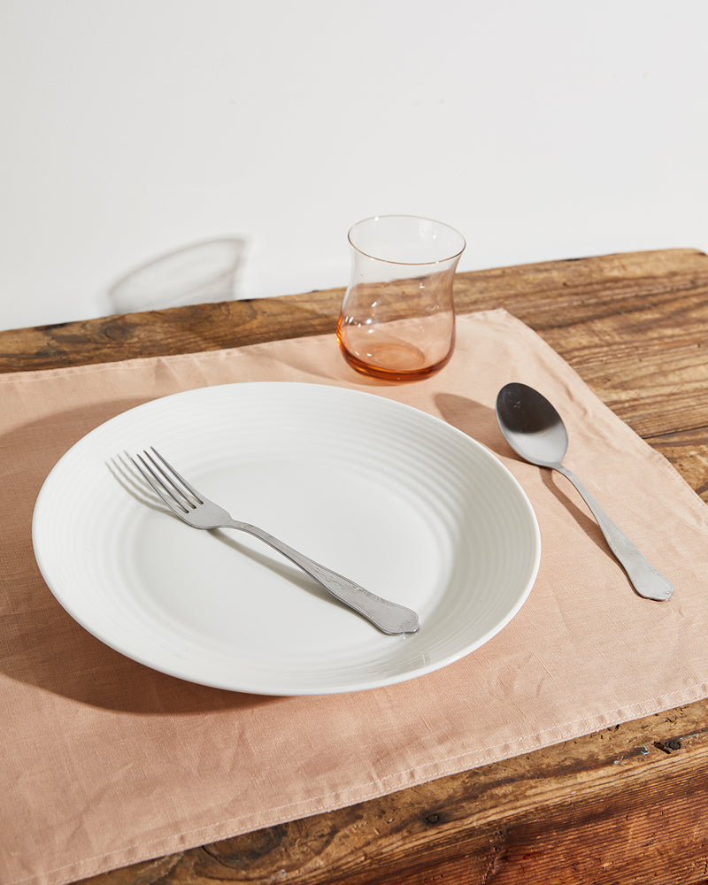 The Hazelnut & Terracotta 100% French Flax Linen Table Bundle by Bed Threads features a white plate with a fork and spoon, a clear glass cup, and classic placemats arranged on a rustic wooden table.