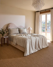 A neatly made bed with a beige upholstered headboard, two Bed Threads Oatmeal & Charcoal 100% French Flax Linen Swirl Pillowcases featuring black trim, and a matching slightly wrinkled French flax linen blanket. - view