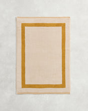 The Bed Threads Crème & Turmeric Two-Toned 100% Cotton Terry Bath Mat features a plush beige center with a bold mustard border, adding cozy style to your space. - view