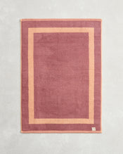 The Bed Threads Terracotta & Pink Clay Two-Toned 100% Cotton Terry Bath Mat, shown flat on a textured surface with a visible corner tag, pairs perfectly with plush towels for a coordinated bathroom style. - view
