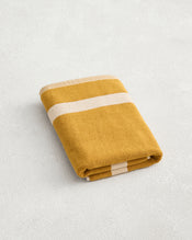 The Bed Threads Crème & Turmeric Two-Toned 100% Cotton Terry Bath Mat features mustard yellow and white stripes, adding a cozy accent to your bathroom when paired with plush towels on a light, textured surface. - view