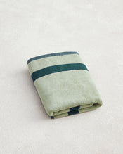 The Forest & Sage Two-Toned 100% Cotton Terry Bath Mat by Bed Threads, featuring light green with two dark green stripes, is neatly folded on a light textured surface. - view