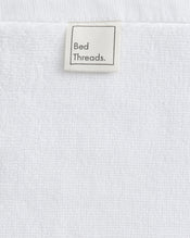 A close-up of Crisp White 100% Cotton Terry Face Washers (Set of Two) from Bed Threads, featuring a beige label and soft, absorbent terry that’s gentle on skin for everyday comfort. - view