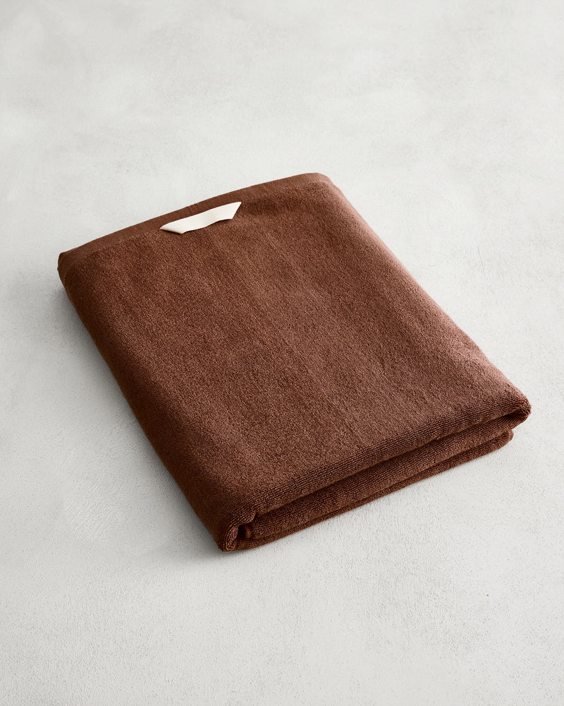 The Bed Threads Espresso 100% Cotton Terry Bath Sheet, neatly folded with a small white tag, rests on a light gray surface.