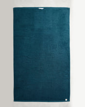 A large, rectangular dark teal Aegean 100% Cotton Terry Bath Sheet by Bed Threads lies flat on a light surface, featuring a white label at the top edge and a sewn-in tag at the bottom—perfect for lovers of luxe cotton towels. - view
