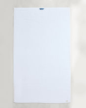 Two Crisp White 100% Cotton Terry Bath Sheets from Bed Threads are laid flat on a light surface, each featuring a small blue loop at the top edge and a discreet tag at the bottom right corner. - view