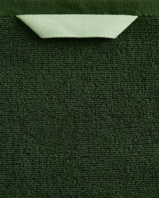 A close-up of the Bed Threads Moss 100% Cotton Terry Bath Sheet Bundle shows its rich dark green texture, with a neatly folded light green corner at the top that reveals the material’s underside.