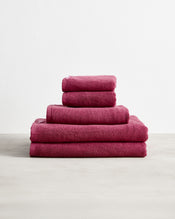 Five Berry 100% Cotton Terry Bath Sheets by Bed Threads are neatly stacked in a pyramid shape on a light surface against a plain white background. - view