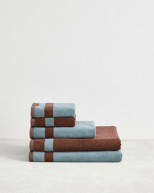 The Bed Threads Cacao & Lagoon Two-Toned 100% Cotton Terry Bath Sheet Bundle features four plush bath towels, neatly stacked from largest to smallest, in alternating blue and brown, displayed on a plain white background.